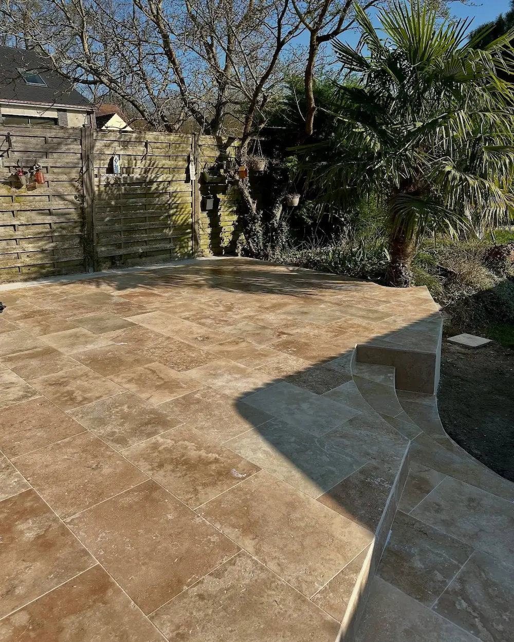 Terrasse rénovée avec un dallage en travertin posé sur dalle béton, finition propre et marches arrondies.