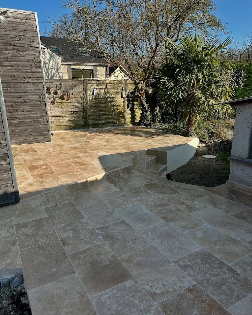 Terrasse rénovée avec un revêtement en travertin posé sur dalle béton, finition après travaux.